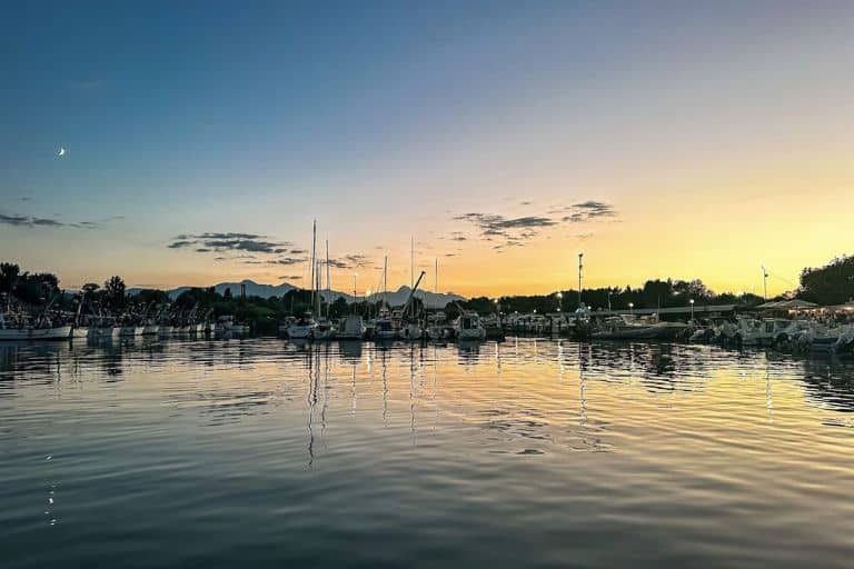 Wide view of a marina at sunset, with sailboats reflected in calm water